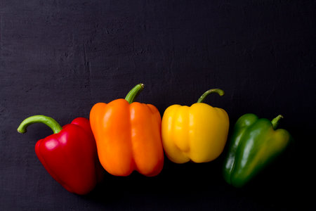 Hand holds red bell pepper close-up on black background.