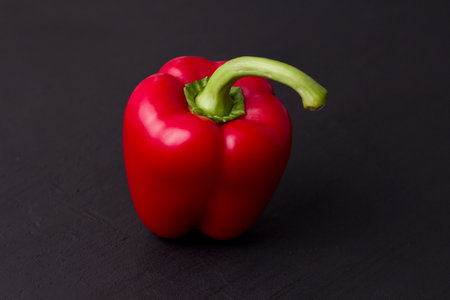 Hand holds red bell pepper close-up on black background.の写真素材