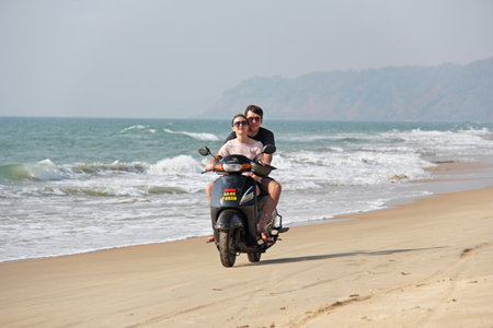 India, GOA, January 22, 2018. A girl and a guy are riding a scooter along the seashore. Scooter on the beach.のeditorial素材