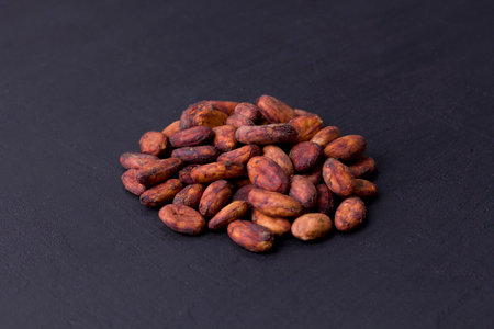 Unpeeled raw brown cocoa beans in heap lie On black modern concrete background. Flat lay, mock up, copy space. Raw materials for making cocoa powder, cocoa beverages, chocolate. Health drink concept.の写真素材