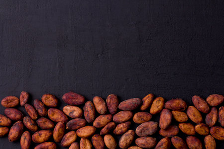 Unpeeled raw brown cocoa beans in heap lie On black modern concrete background. Flat lay, mock up, copy space. Raw materials for making cocoa powder, cocoa beverages, chocolate. Health drink concept.の写真素材