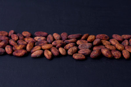 Unpeeled raw brown cocoa beans in heap lie On black modern concrete background. Flat lay, mock up, copy space. Raw materials for making cocoa powder, cocoa beverages, chocolate. Health drink concept.の写真素材