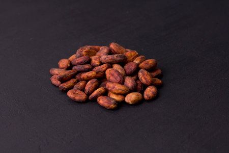 Unpeeled raw brown cocoa beans in heap lie On black modern concrete background. Flat lay, mock up, copy space. Raw materials for making cocoa powder, cocoa beverages, chocolate. Health drink concept.の写真素材