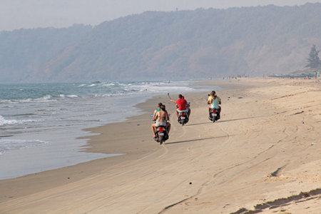 India, GOA, January 22, 2018. A girl and a guy are riding a scooter along the seashore. Scooter on the beach.のeditorial素材