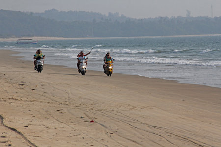 India, GOA, January 22, 2018. A girl and a guy are riding a scooter along the seashore. Scooter on the beach.のeditorial素材