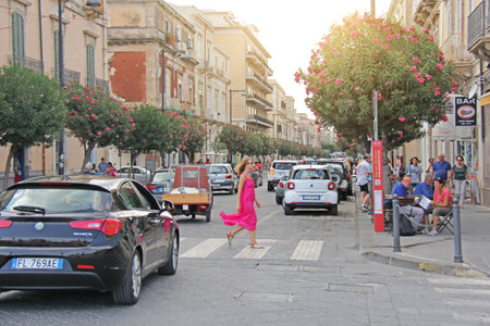 Sicily. Syracuse - October 4, 2017. Young Girl Crosses the Road on the Pedestrian Crossing. In a long Summer Pink Dress. Street Photography. The island of Sicily, Italy.のeditorial素材
