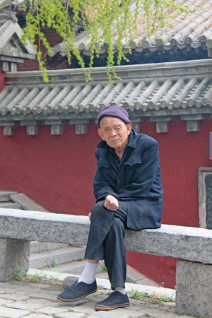 China. Shaolin - April 11, 2012. An old man with big ears and a hat is sitting in the monastery of Shaolin, China.のeditorial素材