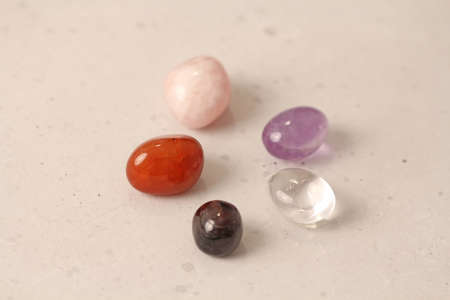 A set of natural stones lies on a light white background, garnet, amethyst, carnelian, rock crystal and rose quartz. Collection of natural stones, mineral and semi-precious stones.の写真素材