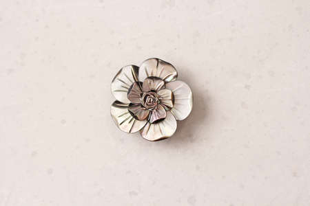 A flower brooch made of natural gray mother-of-pearl lies on a light modern gray white concrete background. Jewelry for women on a light background.の写真素材