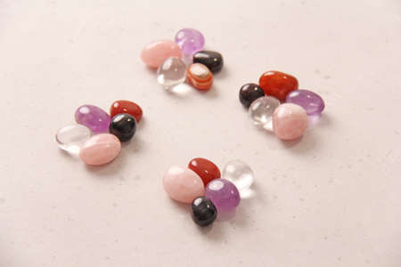 A set of natural stones lies on light white background, garnet, amethyst, carnelian, rock crystal and rose quartz. Collection of natural stones, mineral and semi-precious stones. Smooth round stones.の写真素材