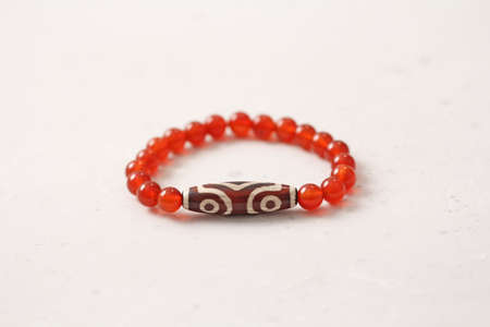 Carnelian stone Dzi bead 3 eyes bracelet. Bracelet made of stones on hand from natural Carnelian. Handmade jewelry bracelets on light background. Tibetan dzi beads 3. Buddhism, fulfillment of desires.の写真素材