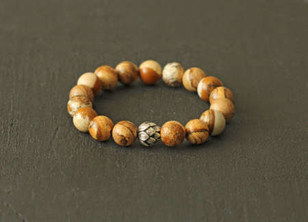 Jasper beige bracelet on elastic with silver bead. Bracelet made of natural stones on hand from natural stone Jasper. Handmade jewelry. Handmade bracelets on black modern background.の写真素材