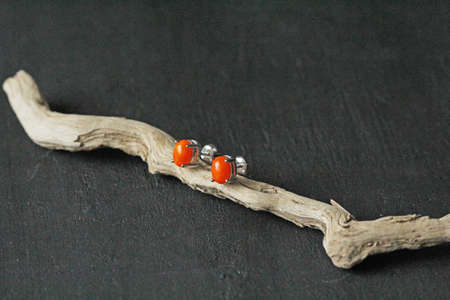 Stud earrings made of natural red coral. Designer earrings from natural red coral stones. Women's jewelry on a black background and wood. Author's modern jewelry. Red earrings studs.の写真素材