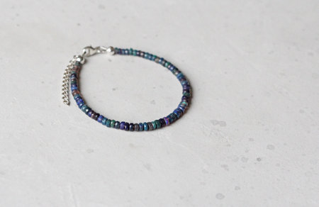 Black fire opal bracelet. Bracelet made of stones on hand from natural stone Black Fire opal. Bracelet made of natural stones. Handmade jewelry. Handmade bracelets on light modern background.の写真素材