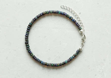 Black fire opal handemade bracelet lies on light background. Bracelet made of natural stones Black fire opal. Handmade jewelry made from natural stones. Modern jewelry on modern concrete background.の写真素材