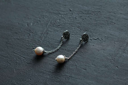 Jewelry long earrings on chains from natural white kasumi pearls and silver. Author's handmade jewelry. Handmade jewelry earrings from natural pearls on black modern concrete background.の写真素材