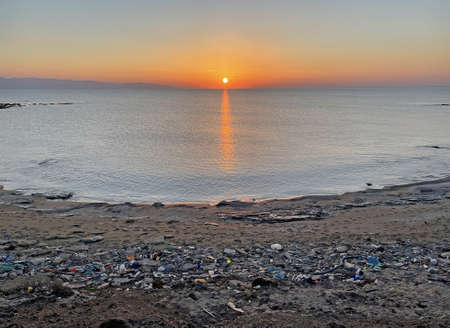 Lot of plastic, garbage, waste lies on seashore, on beach. Environmental disaster in nature. Environmental pollution in North Cyprus. Sunset on the seashore, sun over the sea, sunset on the sea.の写真素材