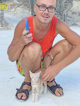 Close-up young handsome man stroking a small blond kitten. Homeless street cats. Care, love, care and tenderness.の写真素材