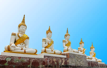 Five white and gold Buddha statue sitting on painted seat base with blue sky background.の写真素材
