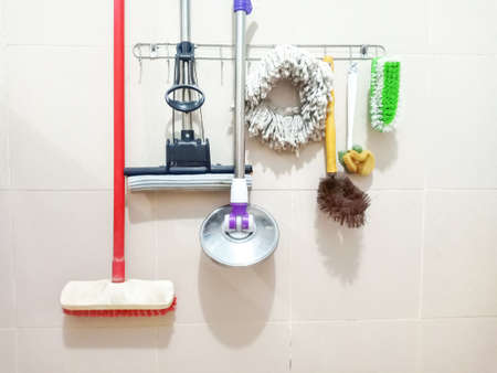 Cleaning equipment hanging on the dirty ceramic restroom wall including toilet brushes and mops.の写真素材