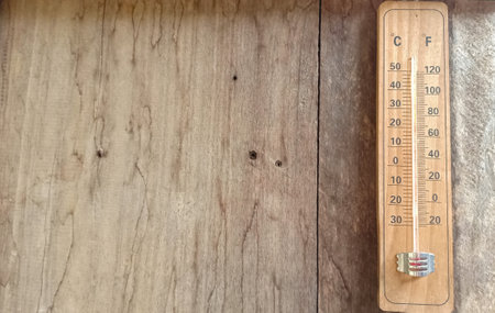 Brown wood thermometer calibrated in degrees celsius and fahrenheit on the gray wooden wall with...