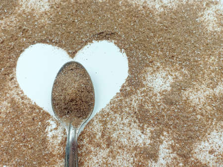 Blurred and rough cocoa powder on spoon with cocoa powder spread around the heart shape on a white background.の写真素材