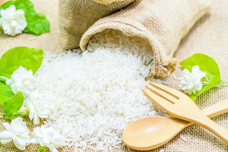 white rice (Thai Jasmine rice) in sack with jasmine flower and wooden spoonの写真素材