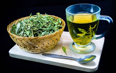 Dry stevia leaves in a small basket and a cup with stevia infusion on blackの写真素材