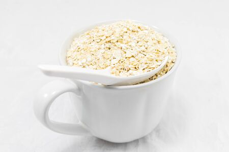 Oat flakes in white cup isolated on white background. Healthy food.の写真素材
