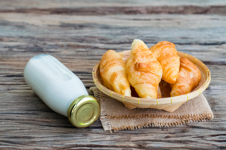 Fresh butter croissants in a bamboo basket with bottle of milk on old woodの写真素材