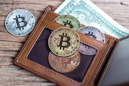Bitcoin and leather wallet with one dollar bill on an old wood background.