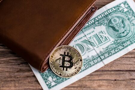 Bitcoin and leather wallet with one dollar bill on an old wood background.
