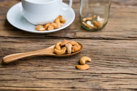 Roasted Cashews in wooden spoon with a white coffee cup on old wood