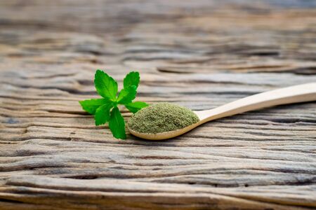 Stevia powder in wooden spoon with fresh green stevia leaves on an old wood background.の写真素材