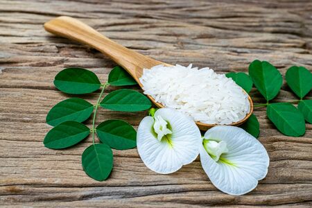 Jasmine rice in a wooden spoon with white anchan flowers on an old wooden tableの写真素材