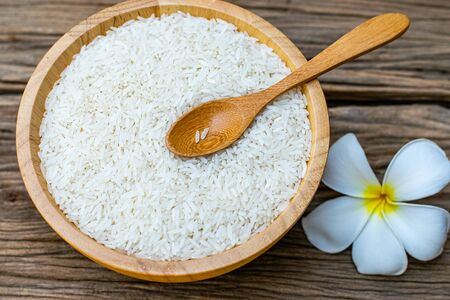 Jasmine rice in a wooden bowl with wooden spoons and plumeria flowers on an old wooden tableの写真素材