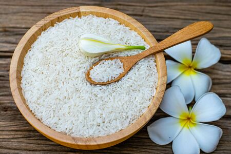 Jasmine rice in a wooden bowl with wooden spoons and plumeria flowers on an old wooden tableの写真素材