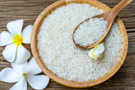 Jasmine rice in a wooden bowl with wooden spoons and plumeria flowers on an old wooden tableの写真素材