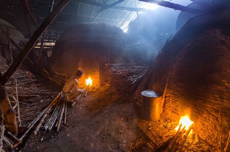 A charcoal worker at work on a pile of slow burning wood charcoal factoryのeditorial素材