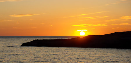 Beach seaside evening at sunset With rocks and hills orange skyの写真素材