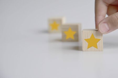 Hand putting wooden cube with five star shape on white background. The best excellent business...