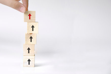Hand of businessman arranging wooden blocks stacking as step with red arrow up on the table, blue background, Business growth success process and development conceptsの写真素材