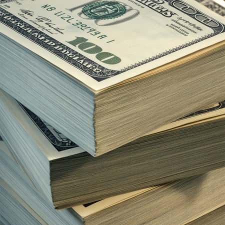A close-up, macro view of several stacks of US hundred dollar bills. The image focuses on the texture and details of the paper currency, with the green ink and intricate designs of the bills visible. The stacks are layered, creating a sense of depth and abundance.の素材