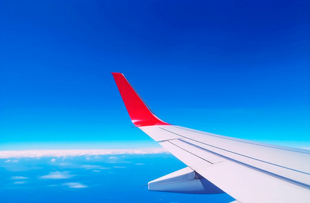 Wing of an airplane flying in the blue sky with white clouds.の素材