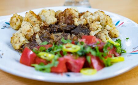 Tasty lunch on a plate. Fried meat slices, cauliflower, hot peppers, tomatoes, parsley