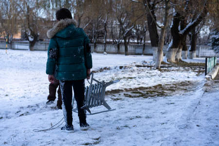 A child in the snow holds a sled in his hands