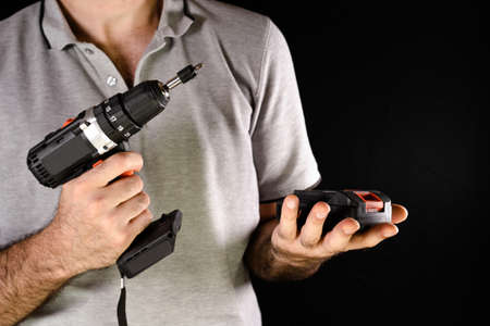 Cordless drill screwdriver. A man holds a battery in his handsの写真素材