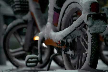 Bicycles coated in thick snow rest in a quiet urban area, reflecting the chilly atmosphere of a winter night with muted lighting highlighting the scene.の写真素材