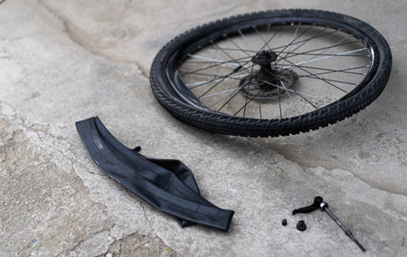 A flat bicycle tire lies next to a damaged inner tube and repair tools on a concrete surface. The maintenance takes place outdoors on a sunny day, highlighting DIY bicycle repair.の写真素材
