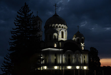 A grand church with domes and crosses stands prominently against a darkening sky, illuminated subtly by soft lights, surrounded by trees, creating a peaceful atmosphere.の写真素材